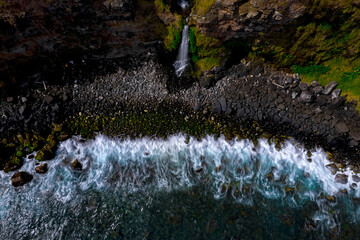 Long exposure aerial view of waves crashing in front of a coastal waterfall located on the south...