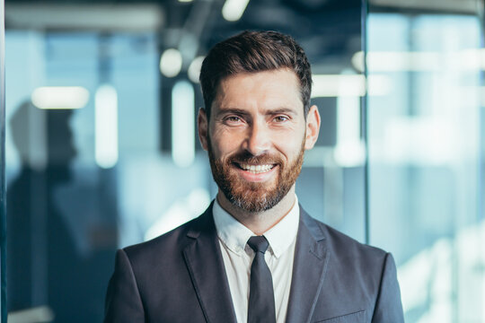 Close-up portrait of businessman with beard looking at camera and smiling, man in modern office