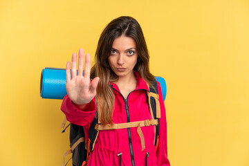 Young mountaineer man with a big backpack isolated on yellow background making stop gesture