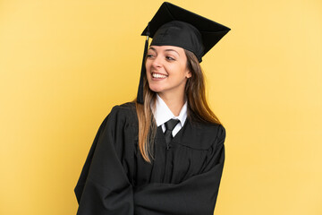 Young university graduate isolated on yellow background looking to the side and smiling