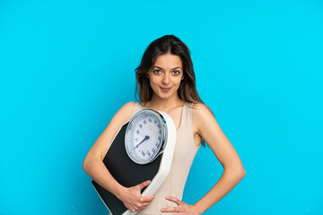 Young caucasian woman isolated on blue background with weighing machine