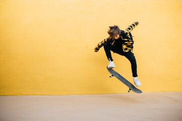 Preteenager student boy jumping with an skateboard in front of a yellow background 