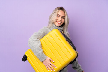 Teenager girl over isolated purple background in vacation with travel suitcase