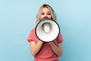 Teenager girl over isolated blue background shouting through a megaphone
