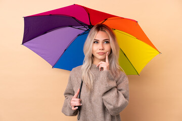 Teenager girl holding an umbrella over isolated background thinking an idea