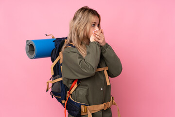 Teenager Russian mountaineer girl with a big backpack isolated on pink background covering mouth and looking to the side