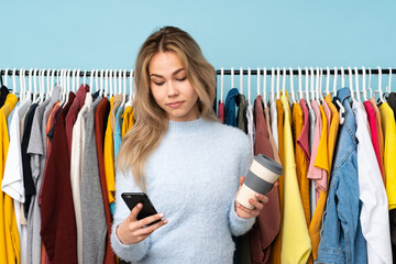 Teenager Russian girl buying some clothes isolated on blue background holding coffee to take away and a mobile