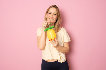 Smiling woman drinking pinapple juice standing isolated over pink background.