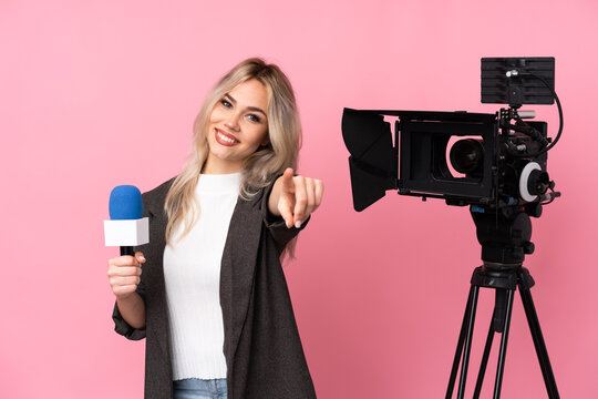 Reporter woman holding a microphone and reporting news over isolated pink background points finger at you with a confident expression