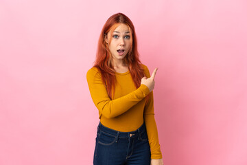Teenager Russian girl isolated on pink background surprised and pointing side