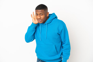 Young latin man isolated on white background listening to something by putting hand on the ear