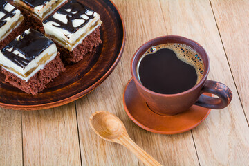 Pieces of delicious chocolate cake with cream and chocolate fondant in a plate and a cup of coffee on a wooden table