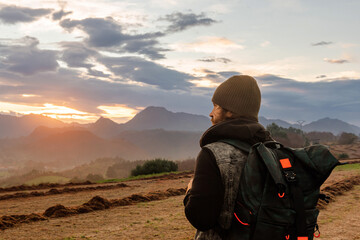 man from behind with backpack contemplating the sunset during a hike in the mountains. travel and healthy lifestyle.