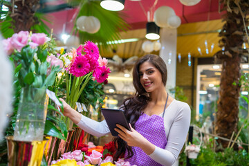 A young florist carefully checks the prices in the flower shop using a tablet