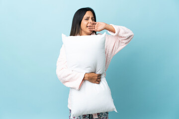 Young woman in pajamas over isolated background in pajamas and holding a pillow and yawning