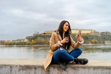 Young beautiful woman using smartphone and drinking coffee takeaway