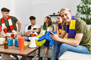Group of young friends watching and supporting soccer match at home.