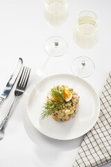 traditional east european dish for New Year's Eve - salad Olivier with potatoes, carrots, onion, peas, sausage, cucumbers, eggs and mayonnaise on a white plate