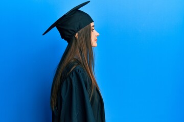 Beautiful brunette young woman wearing graduation cap and ceremony robe looking to side, relax...