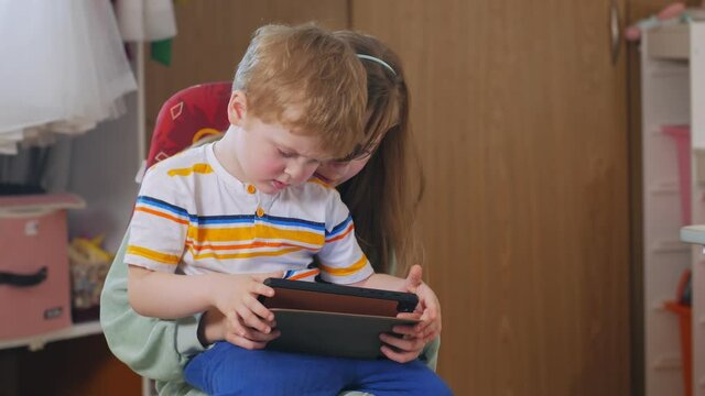 Girl holding a boy on lap brother and sister with tablet