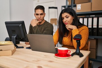 Young woman and man working at small business ecommerce serious face thinking about question with...