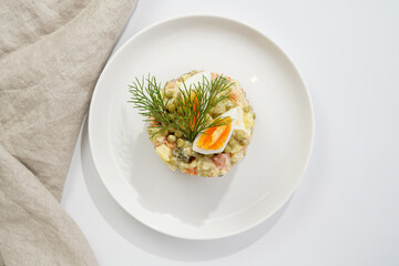 traditional east european dish for New Year's Eve - salad "Olivier" with potatoes, carrots, onion, peas, sausage, cucumbers, eggs and mayonnaise on a white plate