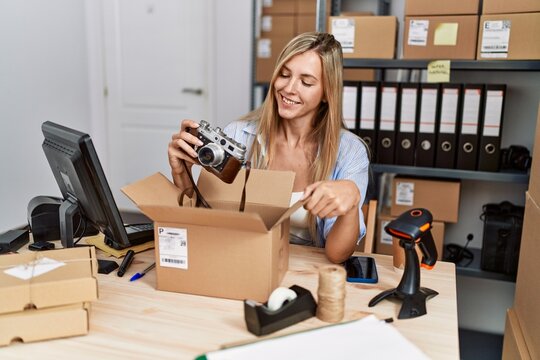 Young blonde woman ecommerce business worker packing vintage camera on order package at office