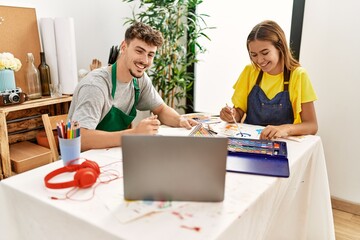 Young hispanic artist couple smiling happy having online draw lesson at art studio.