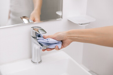 Cleaning the sink faucet with a microfiber cloth. Sanitize surfaces prevention in hospital and public spaces against corona virus. Woman hand using wet wipe. Cleaning the bathroom.