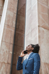 Young afro man in blazer with mobile phone looking up to the sky. Wall background. Vertical copyspace.