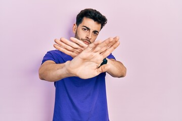 Young hispanic man wearing casual t shirt rejection expression crossing arms and palms doing negative sign, angry face