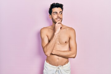 Fototapeta premium Young hispanic man wearing swimwear shirtless with hand on chin thinking about question, pensive expression. smiling with thoughtful face. doubt concept.