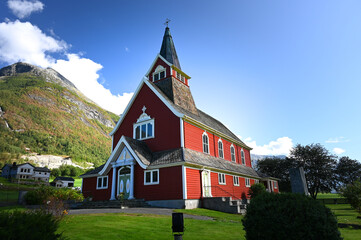 View of the red Olden Church in the village of Olden, Norway on a sunny summer day. Forested...
