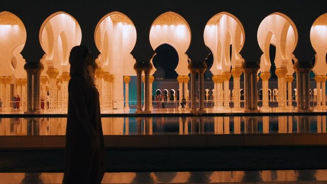 Video with noise. dark black silhouette muslim woman in long dress. Tourist girl walking on night view city, enjoying , admiring beauty modern night illumination, Arabic architecture Islamic styIe.