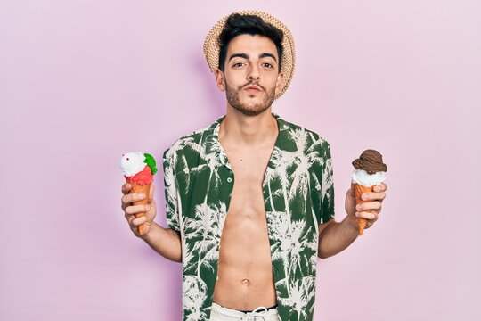 Young hispanic man wearing summer style holding ice cream looking at the camera blowing a kiss being lovely and sexy. love expression.