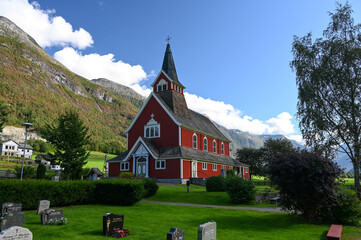 View of the red Olden Church in the village of Olden, Norway on a sunny summer day. Forested...