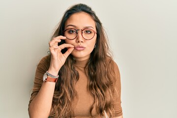 Young hispanic girl wearing casual clothes and glasses mouth and lips shut as zip with fingers....