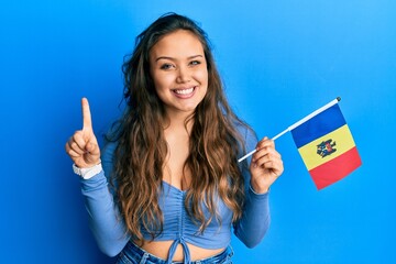 Young hispanic girl holding moldova flag smiling with an idea or question pointing finger with happy face, number one