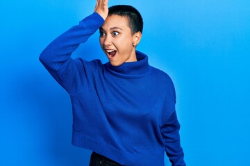 Beautiful hispanic woman with short hair wearing turtleneck sweater surprised with hand on head for mistake, remember error. forgot, bad memory concept.