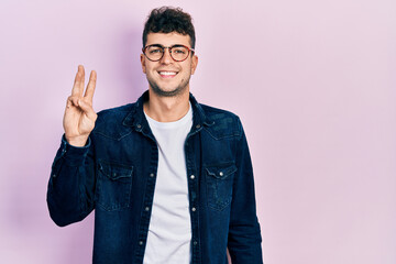 Young hispanic man wearing casual clothes and glasses showing and pointing up with fingers number three while smiling confident and happy.
