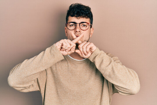Young hispanic man wearing casual clothes and glasses rejection expression crossing fingers doing negative sign