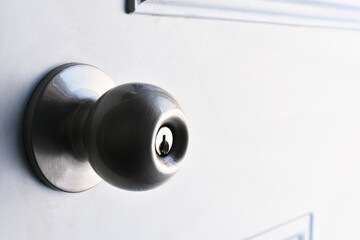 A close up image of a shinny silver exterior door knob on a white metal door. 