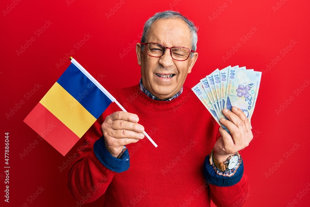 Sticker Handsome senior man with grey hair holding romania flag and leu banknotes winking looking at the camera with sexy expression, cheerful and happy face.