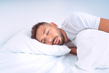 Fototapeta na wymiar Handsome cute man sleeping in the bed with white beddings. Man lying on the pillow and enjoying good healthy sleep