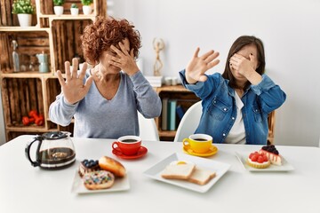 Family of mother and down syndrome daughter sitting at home eating breakfast covering eyes with...