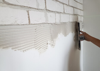 Laying gypsum tiles on plaster glue the wall with a putty knife