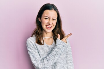 Young brunette woman wearing casual sweater smiling cheerful pointing with hand and finger up to the side