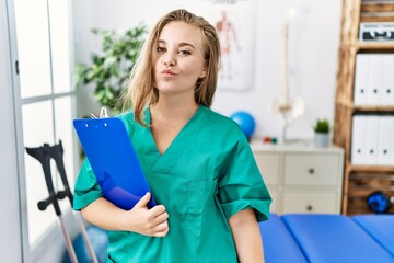 Young caucasian woman working at pain recovery clinic looking at the camera blowing a kiss on air being lovely and sexy. love expression.