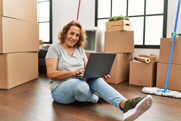 Middle age caucasian woman using laptop sitting on the floor at new home.