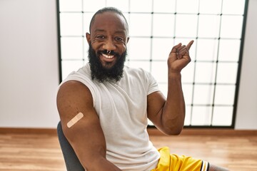 African american man getting vaccine showing arm with band aid smiling happy pointing with hand and finger to the side